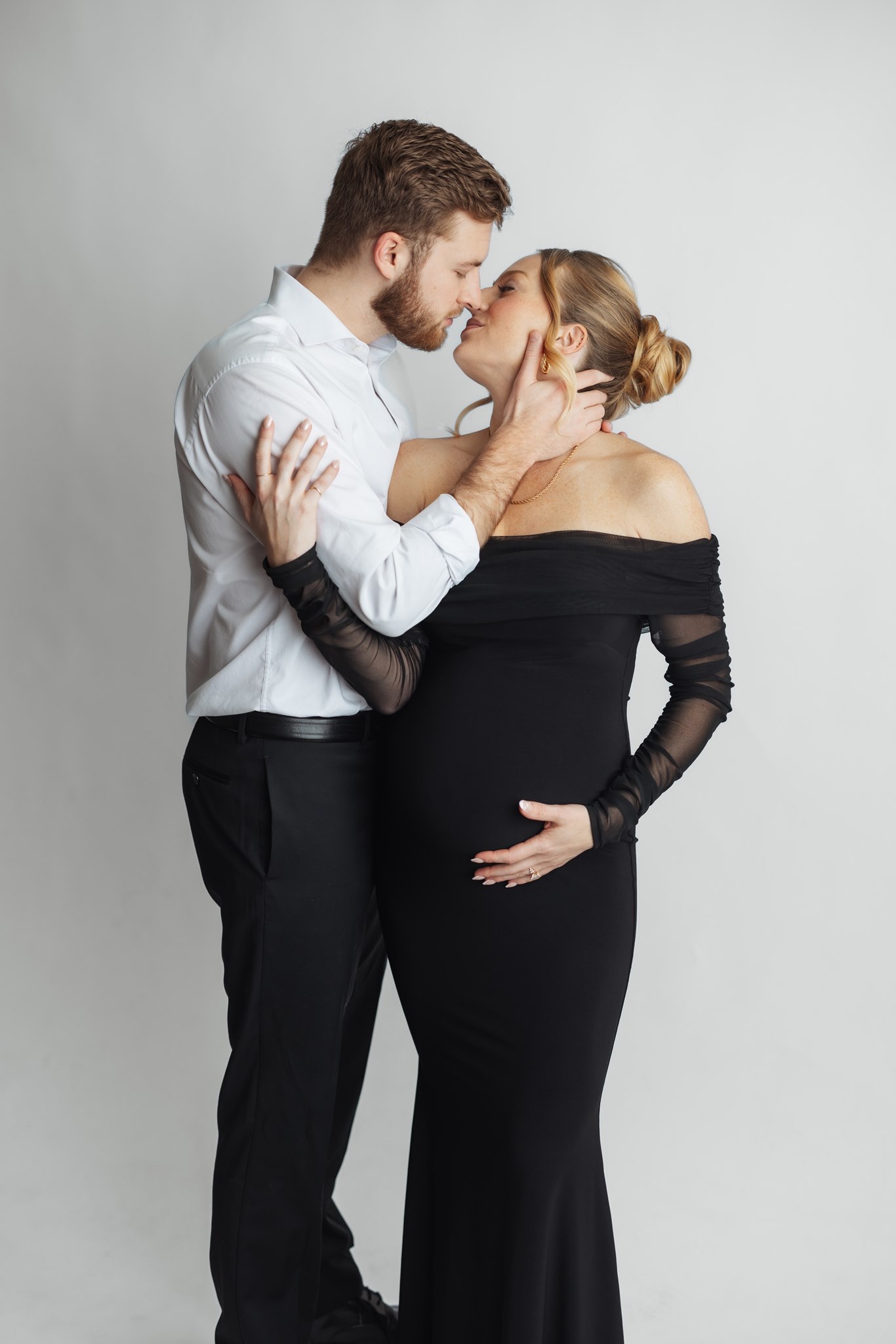 Couple sharing a kiss in the studio, her in an off the shoulder black gown