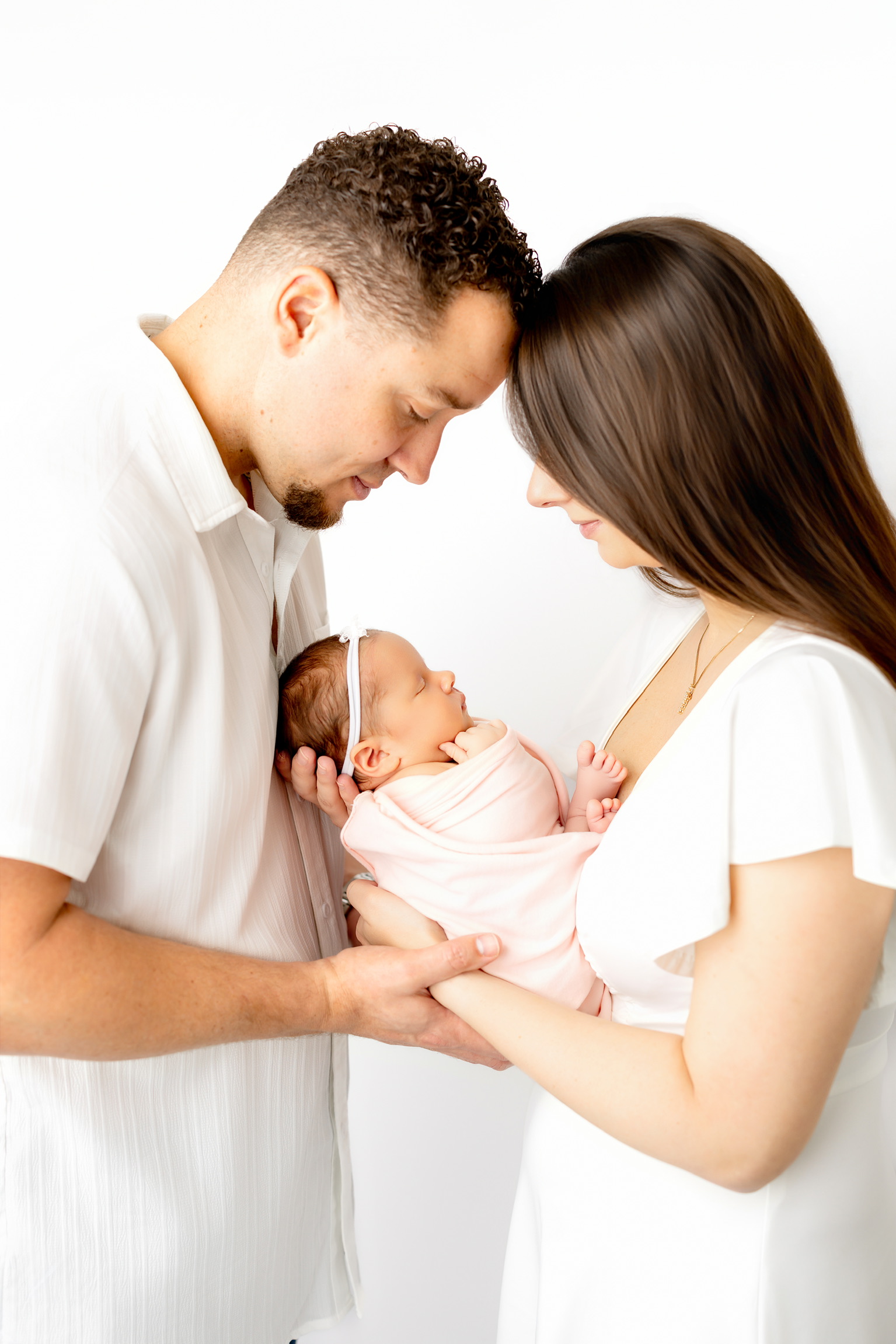 Parents dressed in white holding their newborn daughter between them in a bright studio