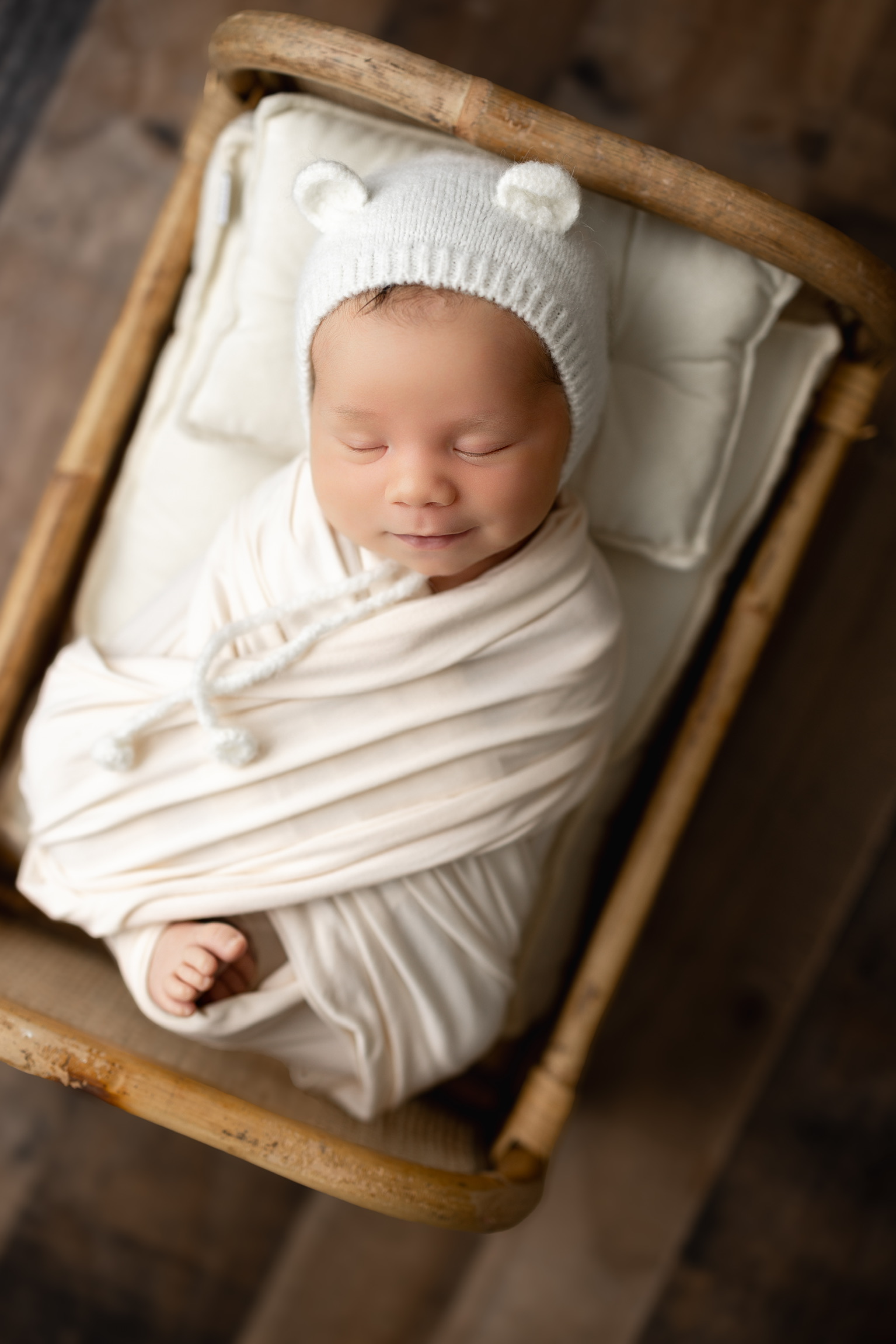 Newborn photography Appleton WI - baby with bear hat in cream wrap, wooden bassinet