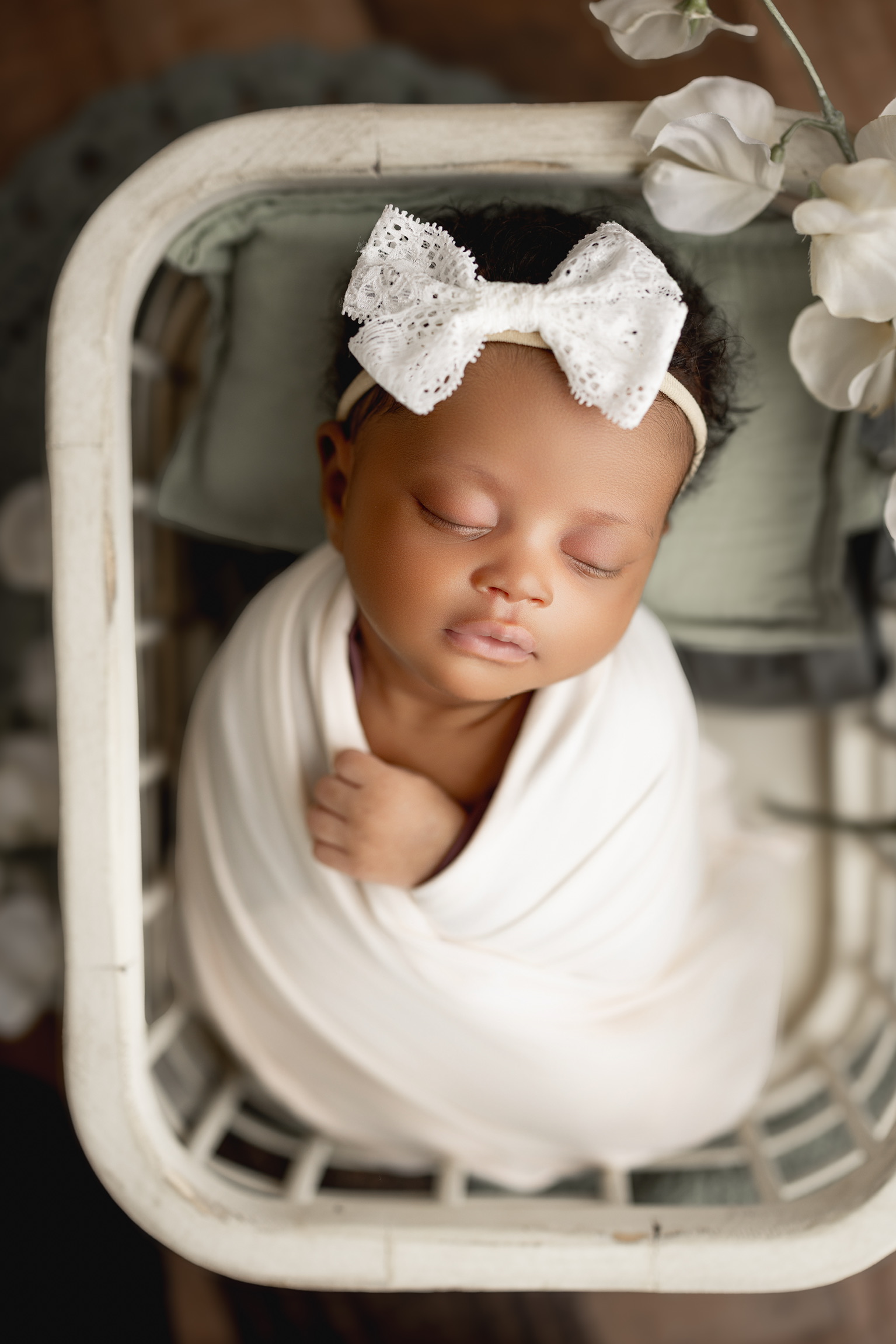 Newborn photography Appleton WI - Black baby girl in white wrap with lace bow and white flowers