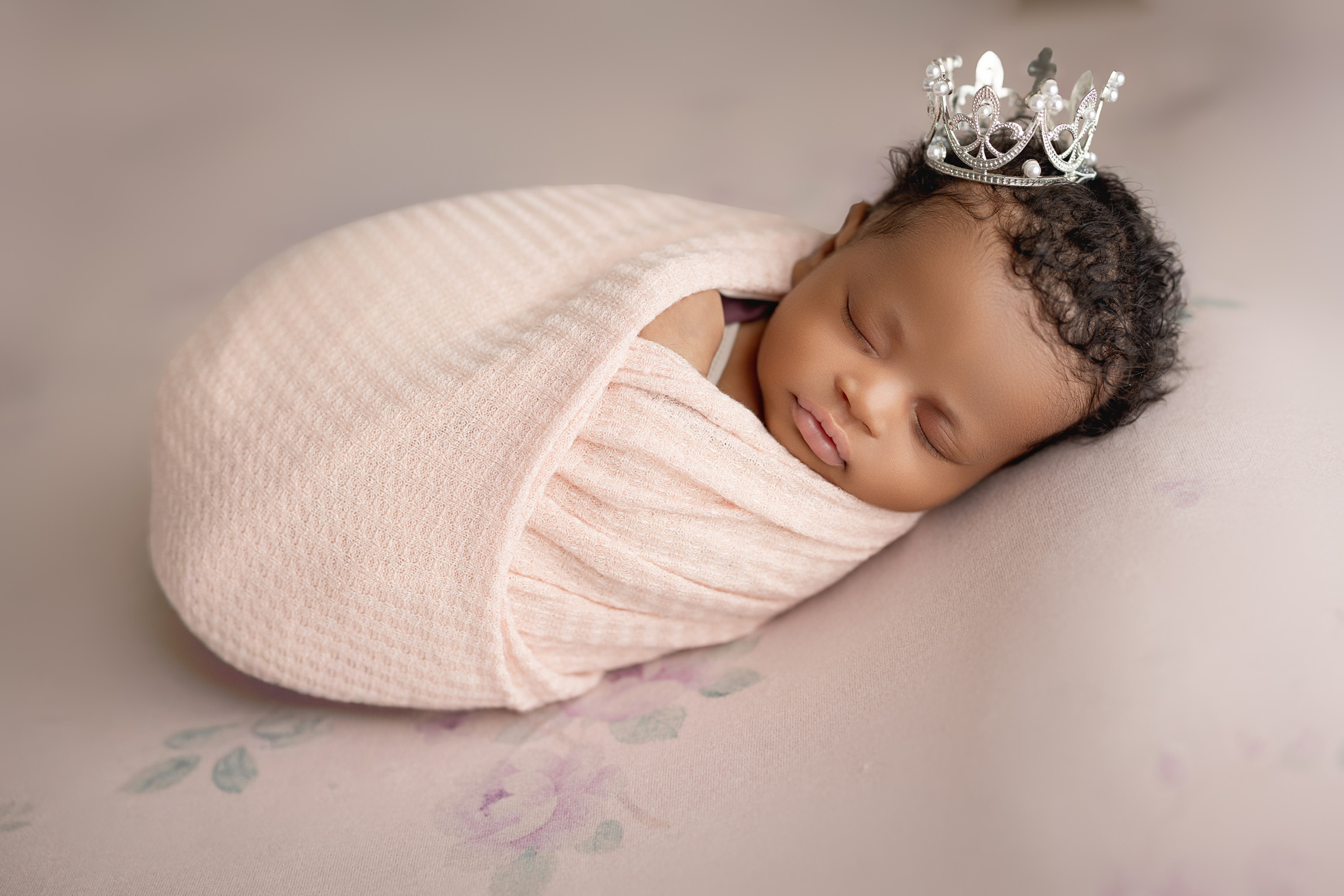 Newborn girl in a pale pink knit wrap wearing a tiny silver crown