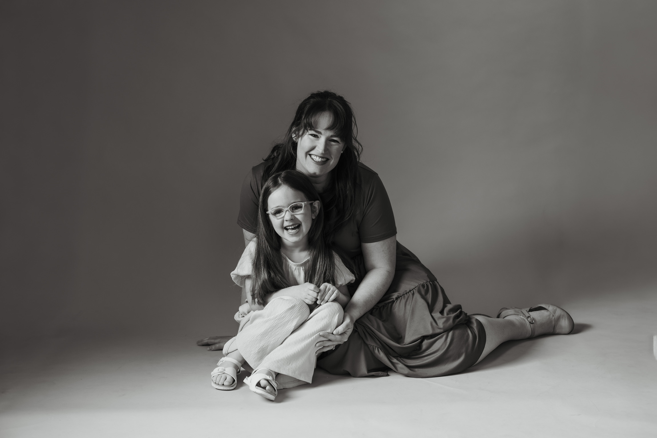 Black and white portrait of a mother and daughter sitting together on the studio floor