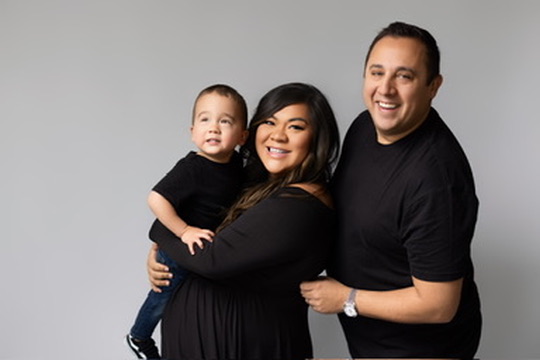 Mom, dad and toddler son laughing together against a gray studio backdrop