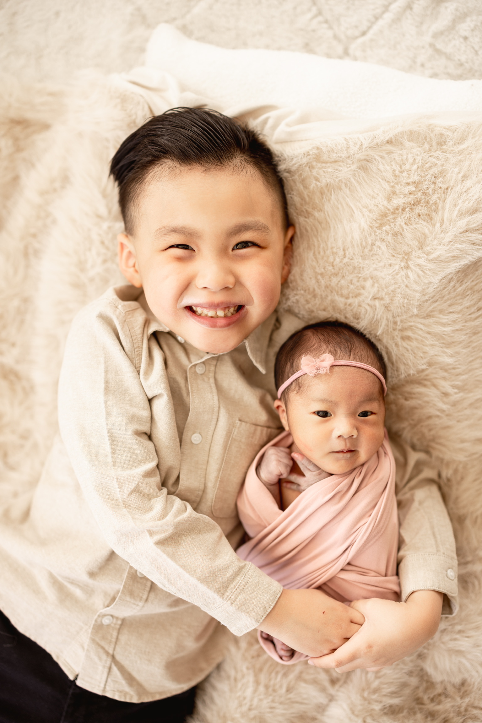 Smiling big brother hugging his newborn sister in a blush wrap and pink headband