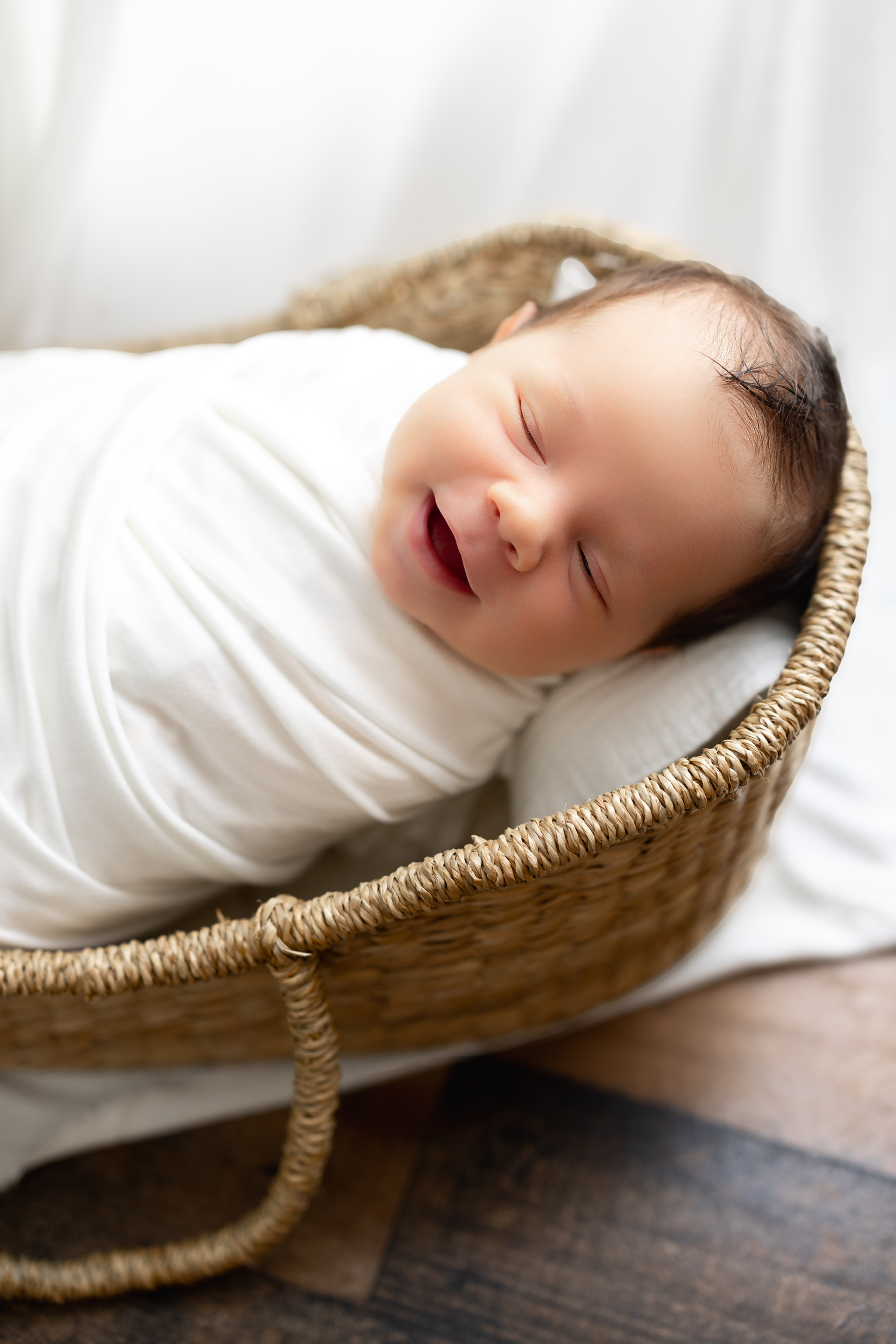Newborn smiling in their sleep, wrapped in white inside a woven basket