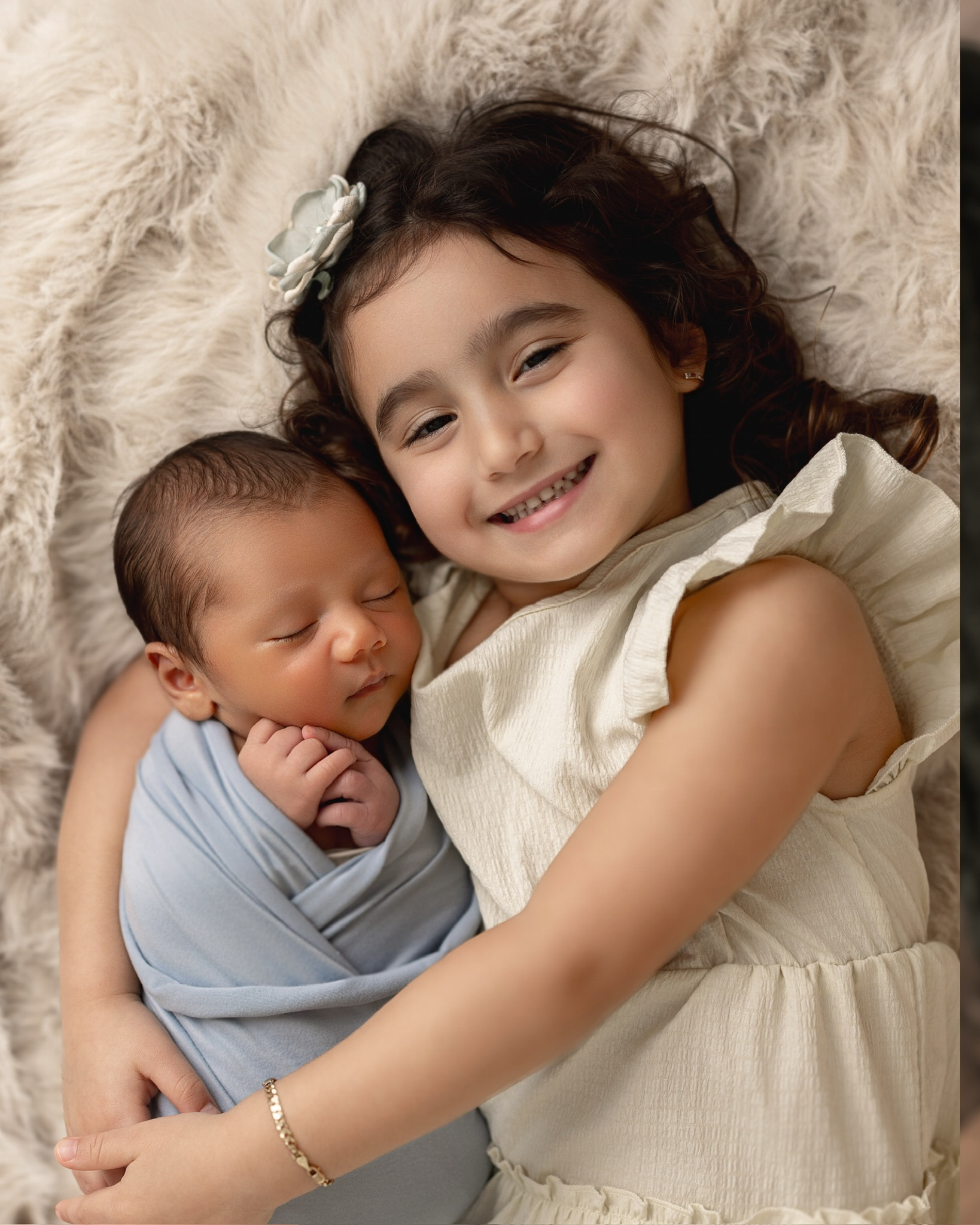 Big sister smiling as she hugs her newborn sibling, wrapped in pale blue