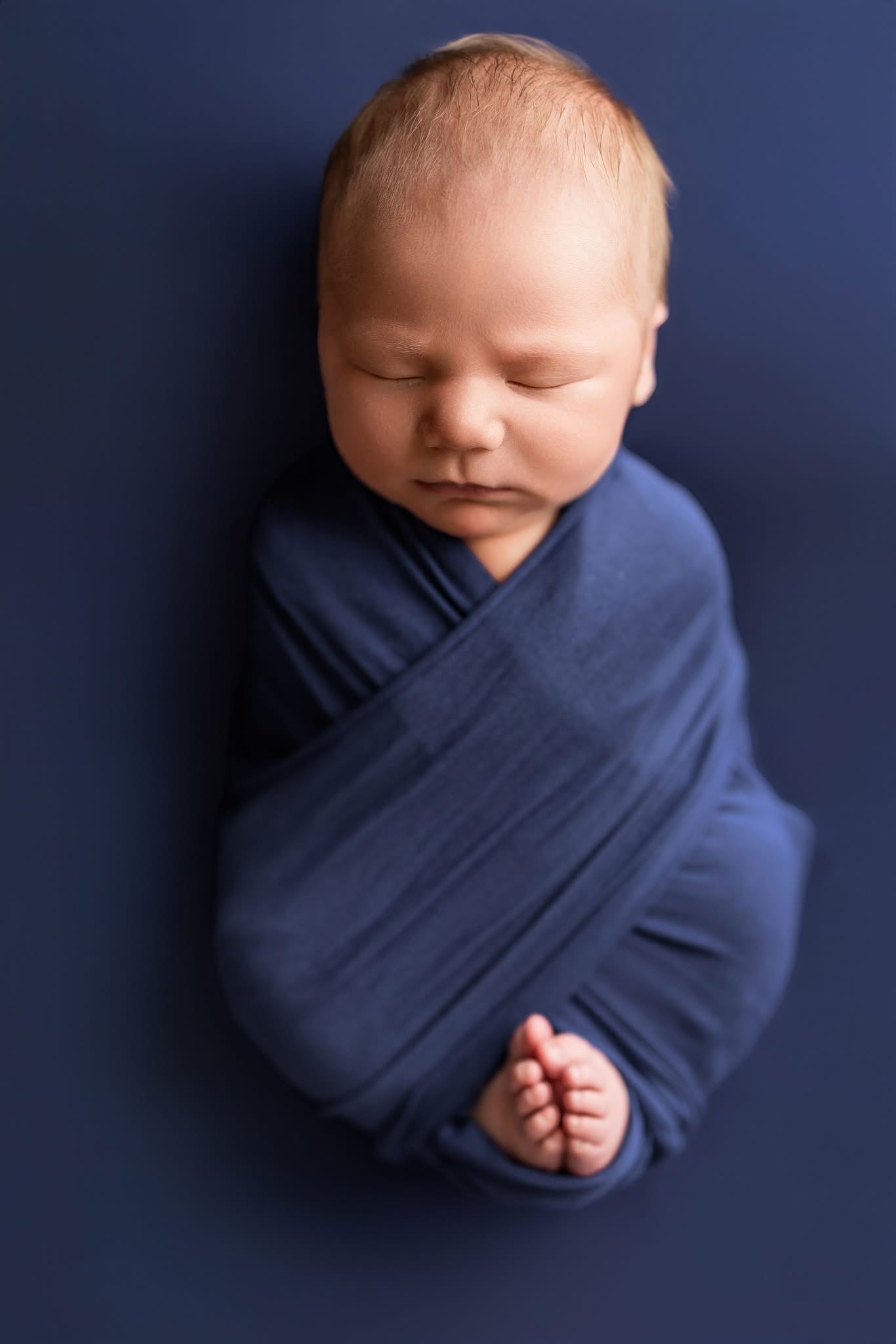 Newborn in a navy blue wrap with tiny feet peeking out at the bottom