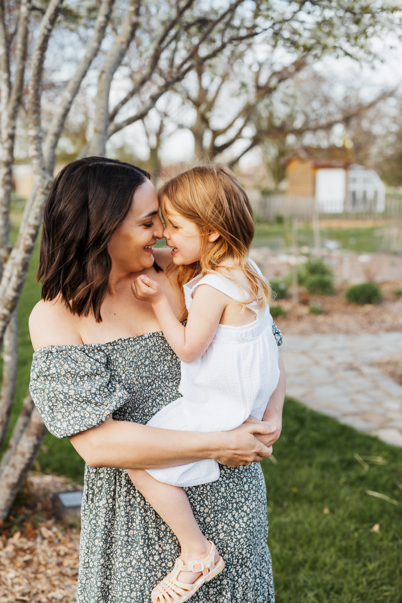 Mother in a green floral dress holding her toddler daughter nose to nose outdoors