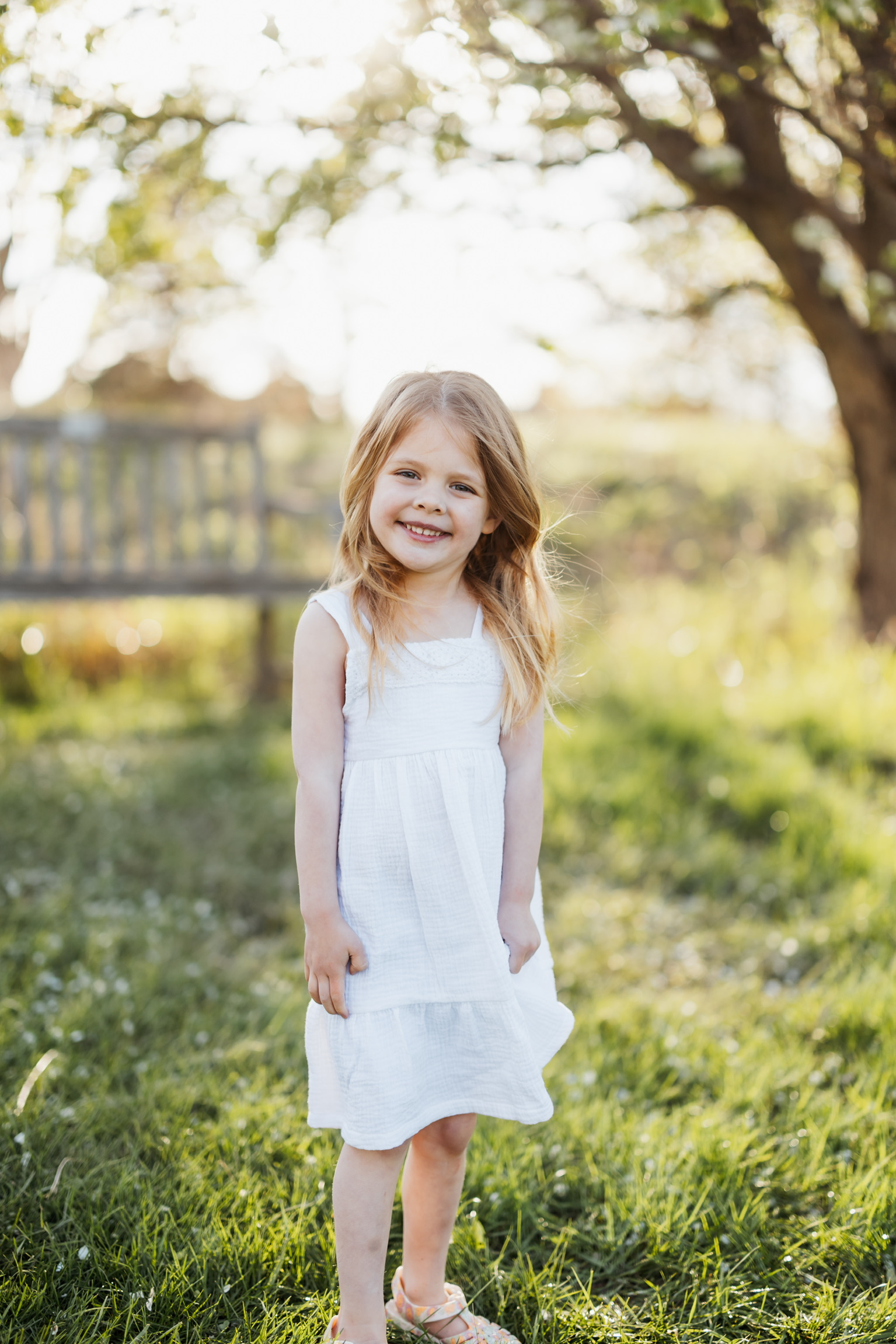 Little girl in a white sundress standing in the grass beneath blossoming trees