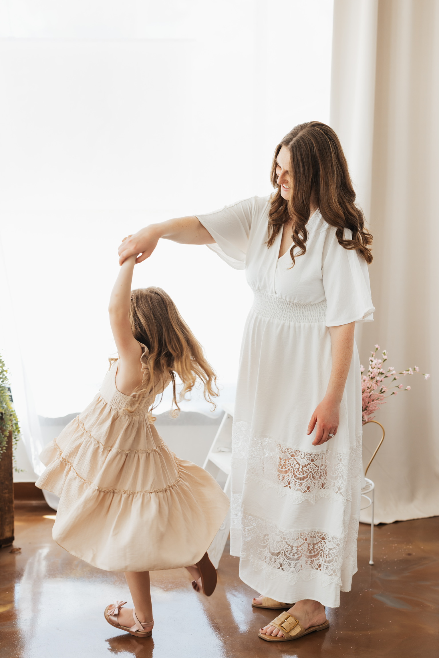 Mother in a white dress twirling her daughter by the hand in a bright studio