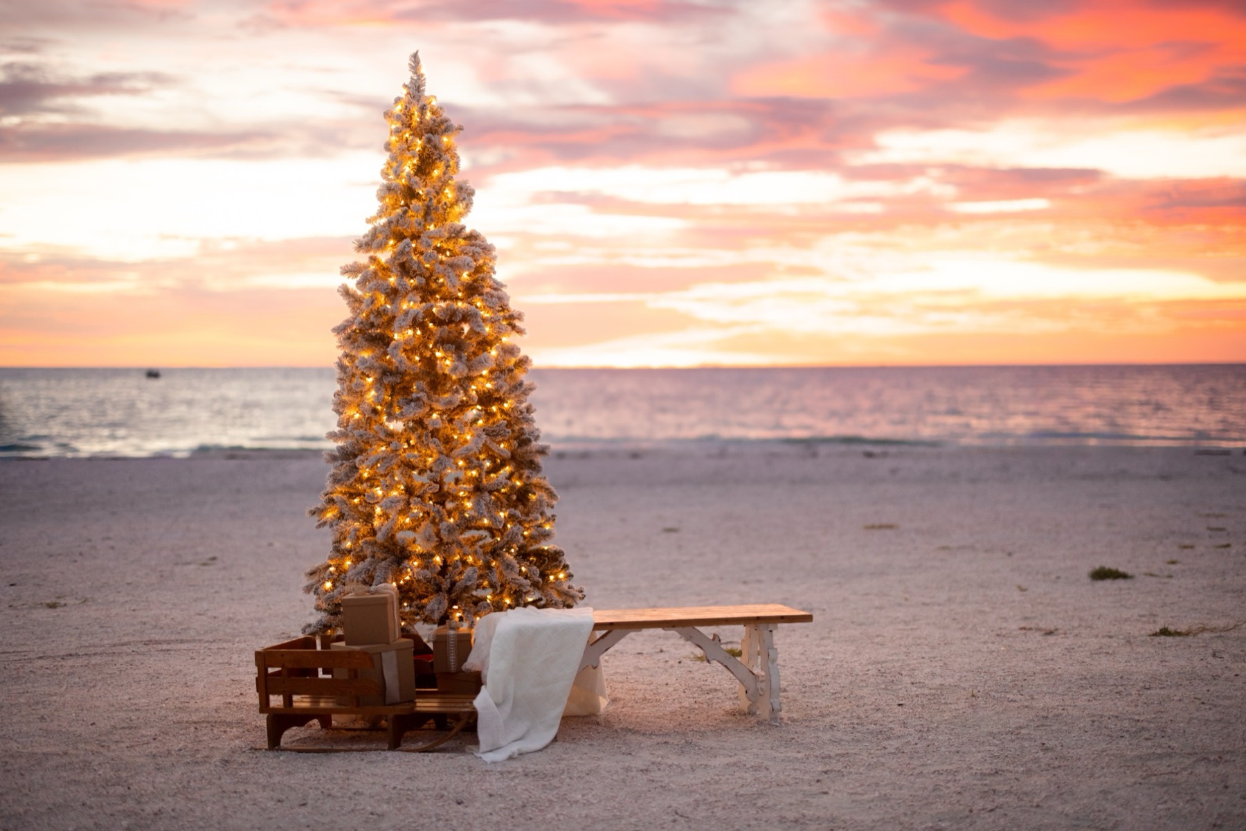 Christmas set on the sand at Pass a Grille beach at sunset with a small lit tree, presents and a cozy blanket